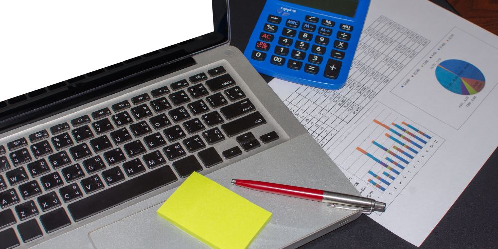 Computador portátil junto a una calculadora y documentos con gráficos.
