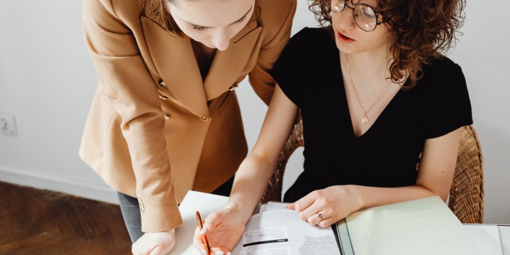 Dos mujeres revisando documentos en una carpeta sobre un escritorio.