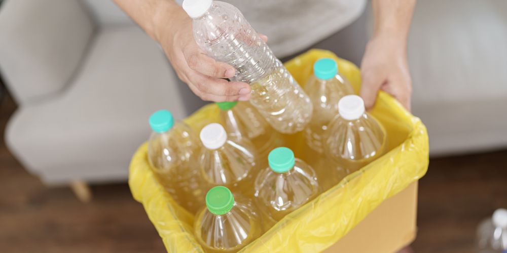 Persona depositando una botella de plástico en un recipiente con otras botellas.