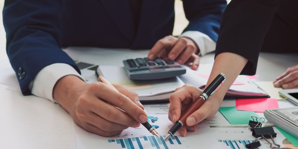 Personas revisando gráficos financieros con bolígrafos y una calculadora sobre la mesa.