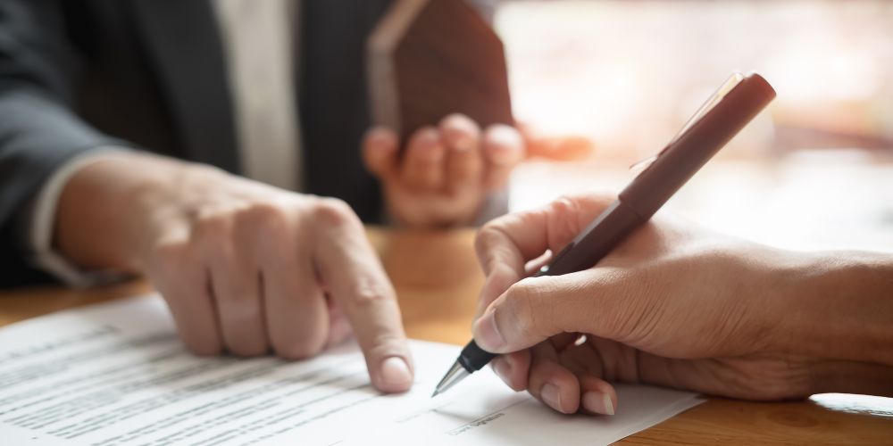 Persona firmando un documento mientras otra señala dónde firmar.