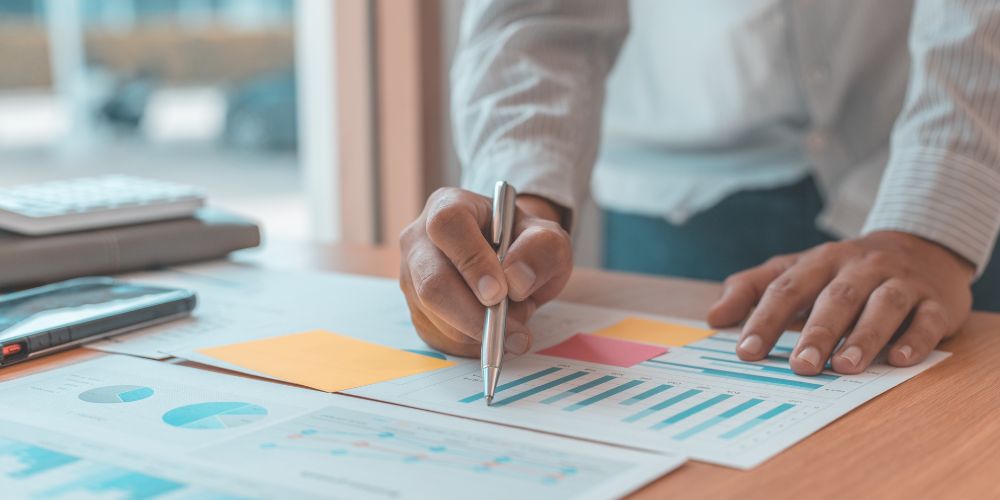 Persona revisando documentos con gráficos sobre un escritorio.