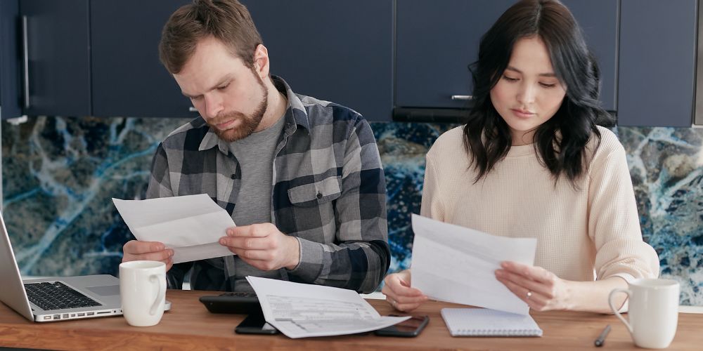 Dos personas revisando documentos en una mesa junto a un computador y una calculadora.