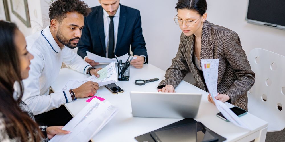 Grupo de personas revisando documentos y gráficos alrededor de un computador portátil.