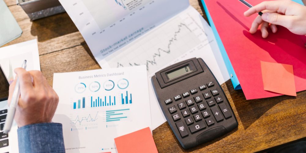 Personas revisando gráficos impresos junto a una calculadora sobre una mesa.