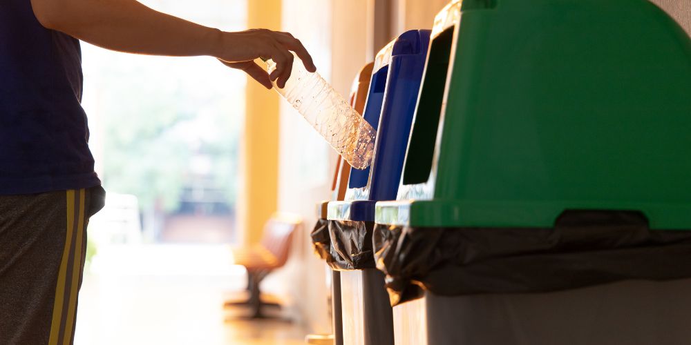 Persona depositando una botella de plástico en un contenedor de reciclaje.
