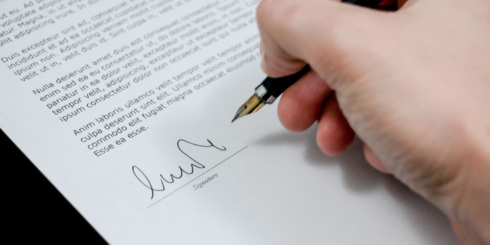 Mano firmando un documento con una pluma estilográfica.