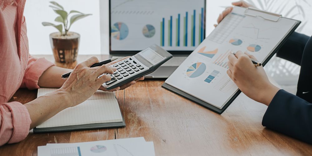 Dos personas revisando gráficos financieros y utilizando una calculadora.