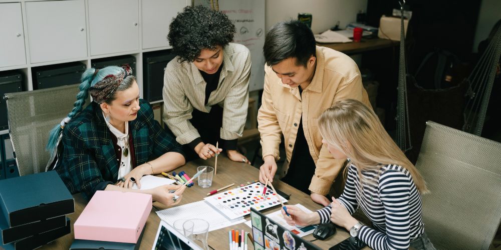 Cuatro personas trabajando alrededor de una mesa con muestras de colores y materiales de diseño.