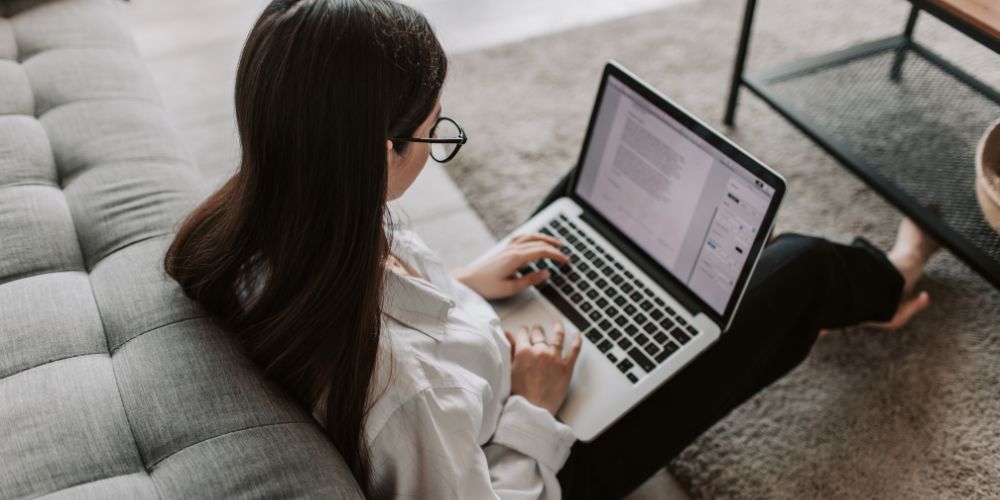 Mujer sentada en un sofá trabajando con un computador portátil.