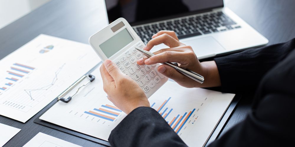 Revisión de informes financieros con calculadora y computador como parte de la regularización contable.