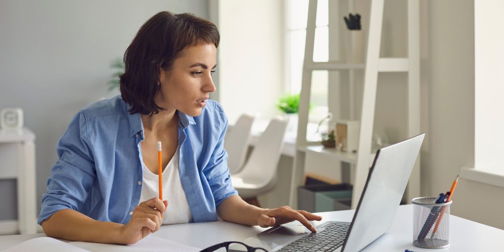 Mujer estudiando frente a un computador portátil con lápiz y cuaderno.