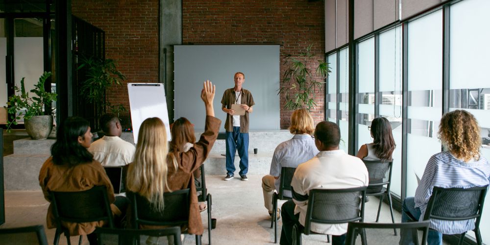 Adultos participando en un taller presencial, con una asistente levantando la mano.