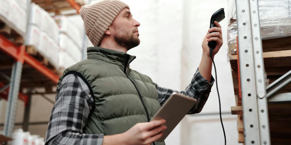 Trabajador utilizando un lector de códigos y una tablet para controlar mercancías en una bodega
