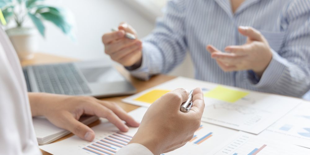Dos personas revisando informes con gráficos durante una reunión de asesoría.