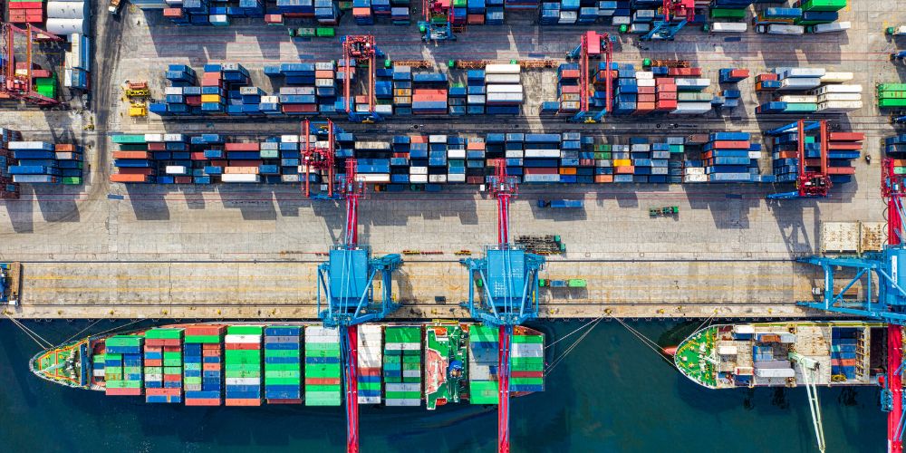 Vista aérea de buques portacontenedores y grúas en una terminal de comercio internacional.