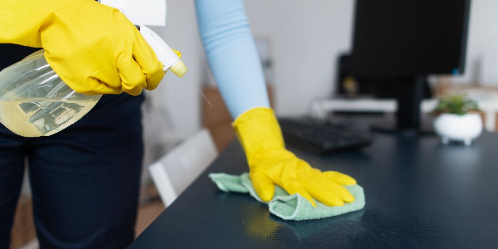 Limpieza de un escritorio de oficina con guantes, paño y pulverizador.
