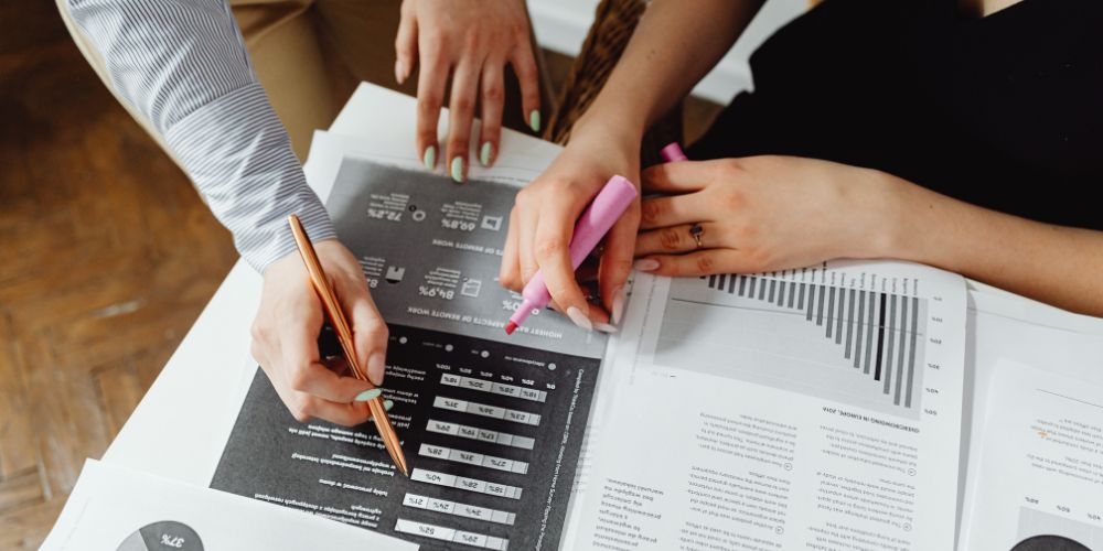 Personas revisando informes impresos con gráficos, un lápiz y un destacador.