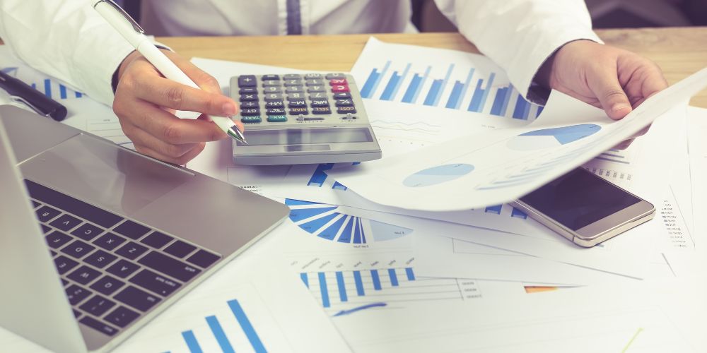 Revisión de informes financieros con gráficos, calculadora y computador portátil.