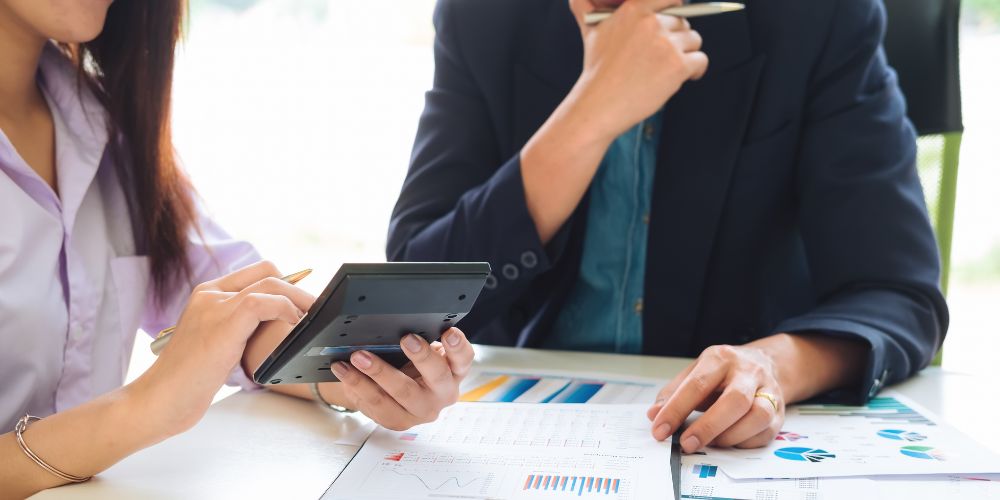 Dos personas revisando informes contables y gráficos con una calculadora.