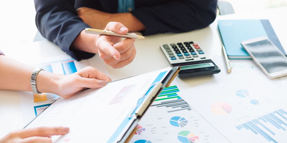 Personas revisando informes con gráficos junto a una calculadora y un teléfono móvil.