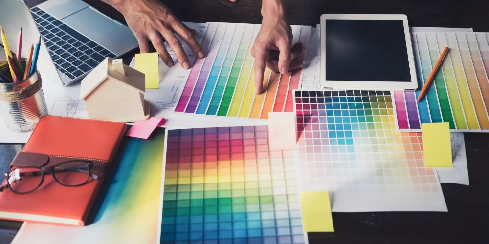 Selección de una paleta de colores sobre una mesa con muestras, computador y tablet.