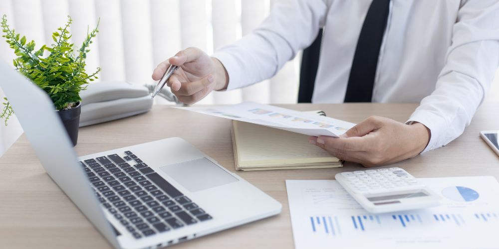 Revisión de informes financieros con computador y calculadora para la contabilidad de una pyme.