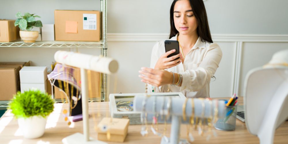 Mujer fotografiando joyas con un teléfono para crear contenido de marketing para joyerías.