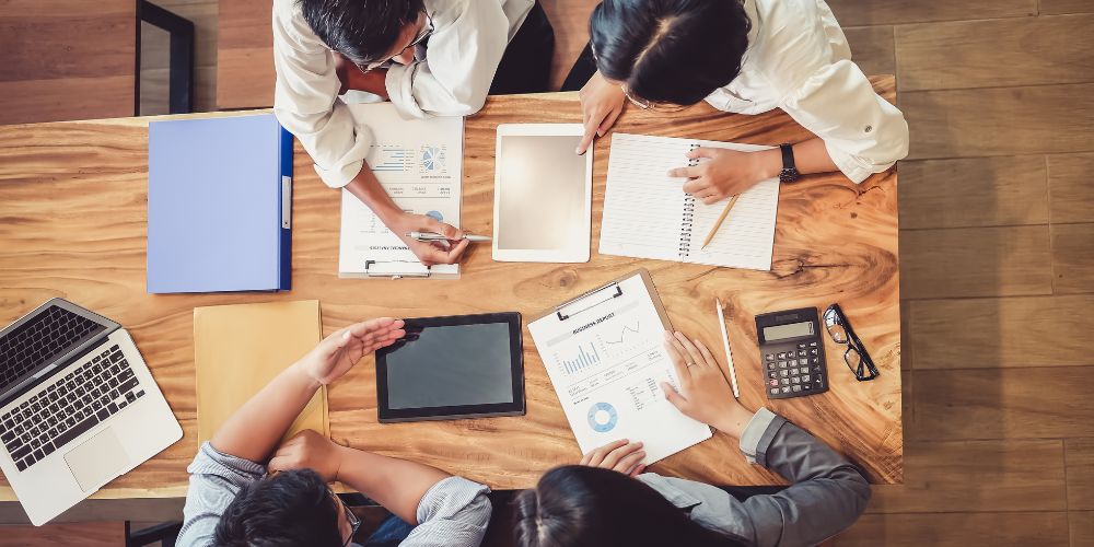 Cuatro personas reunidas alrededor de una mesa con tablets, documentos y gráficos.